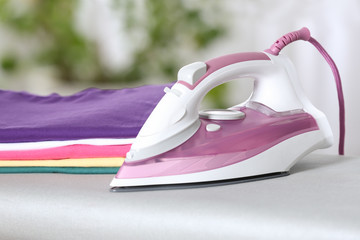 Modern electric iron and clean folded clothes on board indoors