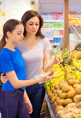 Teen girl with mother shopping in the supermarket at the fruit section. Choosing daily product. Concept of healthy food, bio, vegetarian, diet.