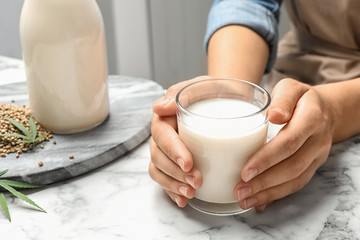 Woman with glass of hemp milk at white marble table, closeup