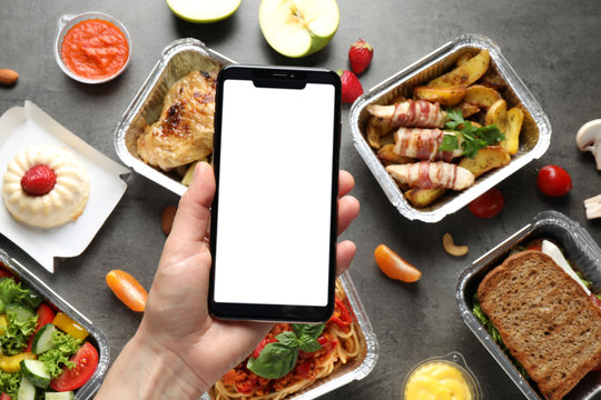 Top view of woman holding smartphone over grey table with lunchboxes, mockup for design. Healthy food delivery