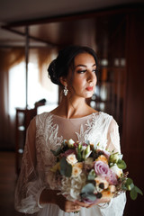 Beautiful bride with a wedding bouquet. Pretty woman with professional make up and hair style. Stylish happy bride is getting ready in the morning. Wedding day. Fashion bride.