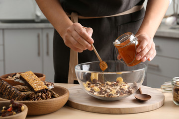 Woman preparing healthy granola bar at wooden table in kitchen