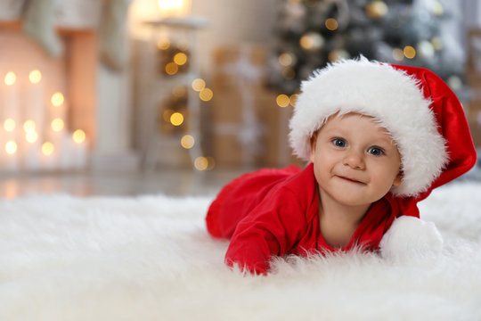 Little baby wearing Santa hat on floor at home. First Christmas