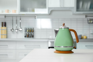 Modern electric kettle on wooden table in kitchen. Space for text