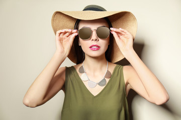 Beautiful woman in stylish sunglasses and hat on beige background