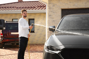 Young happy man washing car at backyard on sunny day