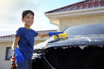 Happy little boy washing car at backyard on sunny day