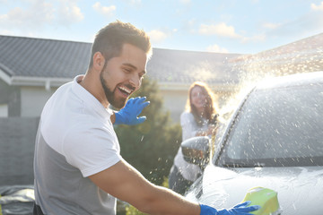 Happy couple washing car and having fun at backyard on sunny day