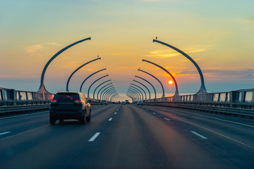 Obraz premium Expressway. Traffic on the bridge. Cars go against the background of the setting sun. Road infrastructure. Travel by car. Road home. Motorway in the evening.