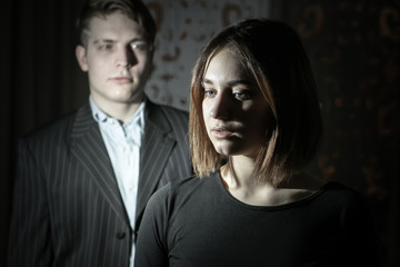 A man and a girl in dark clothes on a dark background. Problem in relations. Incomprehension. Alienation. Divorce. Lack of joy from communication. Sadness.