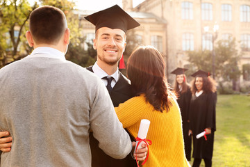 Happy student with parents after graduation ceremony outdoors