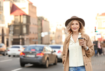 Fototapeta premium Mature woman with cup of coffee on city street