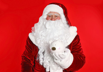 Santa Claus holding piggy bank on red background