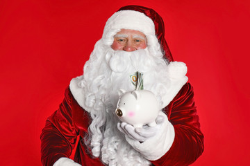 Santa Claus holding piggy bank with dollar banknotes on red background