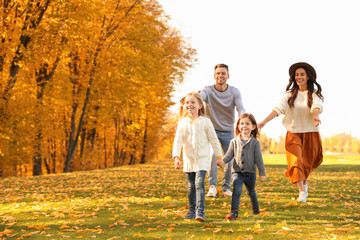Naklejka na ściany i meble Happy family with little daughters having fun in park. Autumn park
