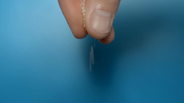 Male hand, fingers profusely salting something on blue background hd stock footage