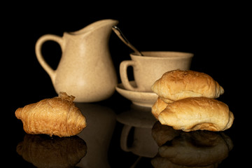 Group of four whole fresh baked mini croissant with ceramic jug and cup isolated on black glass