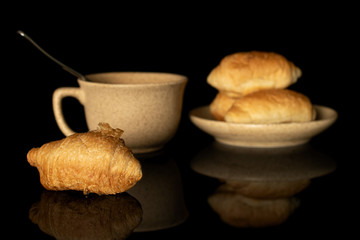 Group of four whole fresh baked mini croissant with cup and saucer isolated on black glass