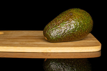 One whole fresh green avocado on bamboo cutting board isolated on black glass