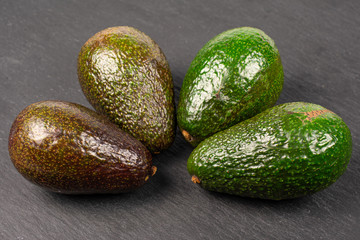 Group of four whole fresh green avocado on grey stone