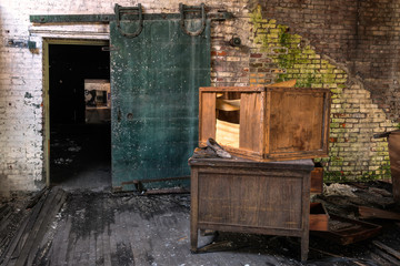 Fototapeta na wymiar Interior of a room with and old desk, broken crate, moldy brick walls, and an interesting green door. Image taken at the old Scranton Lace Factory, built in 1890, closed in 2002, demolished in 2019.