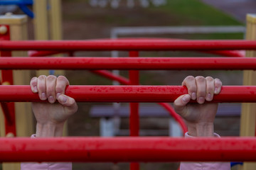 Girl hanging bar by 2 hands the outdoor exercise equipment. In public park, soft focus