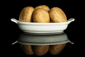 Group of four whole fresh brown champignon in white oval ceramic bowl isolated on black glass