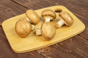 Group of five whole fresh brown champignon on bamboo cutting board on brown wood