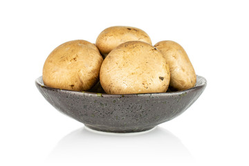 Group of four whole fresh brown champignon in dark ceramic bowl isolated on white background