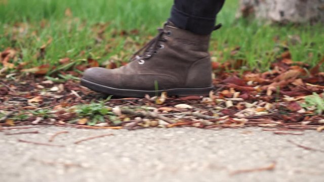 Young man in leather shoes is walking along a path with fallen leaves. Fall season. Outdoor city walk concept slow motion .