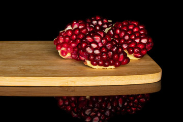 Group of four pieces of fresh red pomegranate on bamboo cutting board isolated on black glass