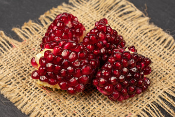 Group of four pieces of fresh red pomegranate on natural sackcloth on grey stone