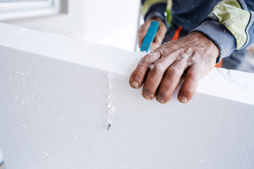 Construction worker using the hand saw to cut the styrofoam insulation panel table at the construction site in the insulating renovation procedure