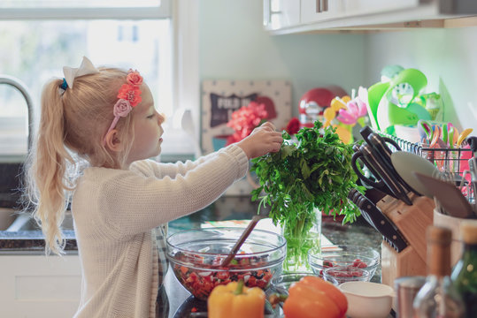 Little girl adding fresh parsley to a salad - kids in the kitchen