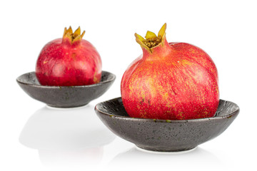 Group of two whole fresh red pomegranate in dark ceramic bowl isolated on white background