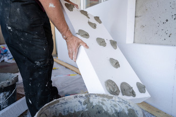 Worker hand holding panel with applied cement adhesive glue on white on styrofoam wall insulation...