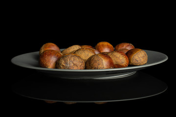 Lot of whole sweet brown chestnut on gray ceramic plate isolated on black glass