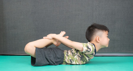 An Asian boy is doing yoga for children at his own home.