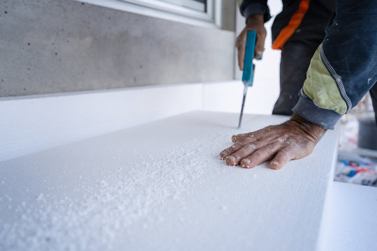 Construction worker using the hand saw to cut the styrofoam insulation panel table at the construction site in the insulating renovation procedure