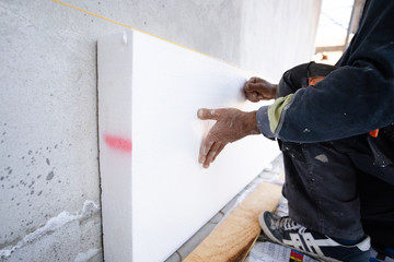 Worker placing styrofoam sheet insulation to the wall at construction site Rigid extruded...