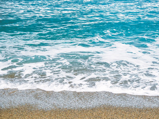 beautiful view on the seashore with stones and sand, soft waves with foam, blue and turquoise water. summer vacation and tourism concept