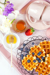 Modern blush pink breakfast tray with waffles, honey and fruit, vertical flat lay close up.