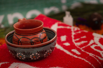 a handmade clay mexican pot decorated with traditional mexican drawings on a handmade mexican orange poncho