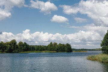 Summer lake in forest landscape. Blue cloudy sky over water surface panoramic view.