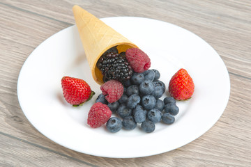 Different fresh berries in a waffle glass on a white plate. Vitamin and healthy food.