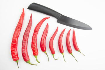 Red hot pepper and black ceramic kitchen knife on white background. Healthy vegetable food and vitamins.