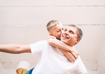 Boy blond schoolboy 8 years old with his young father, the child sits on top and hugs his father. Time together, family, single parent. Father's day