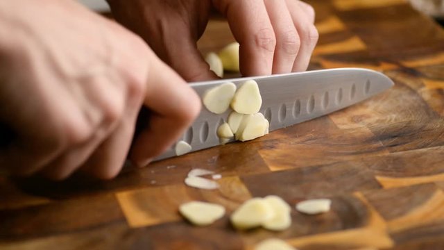 Arc Shot Of Chef Slicing A Clove Of Garlic On A Wood Cutting Board