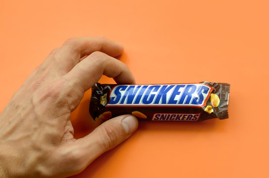 Hand Holding A Snickers Chocolate Bar. Snickers Bars Are Produced By Mars Incorporated. Snickers Was Created By Franklin Clarence Mars In 1930