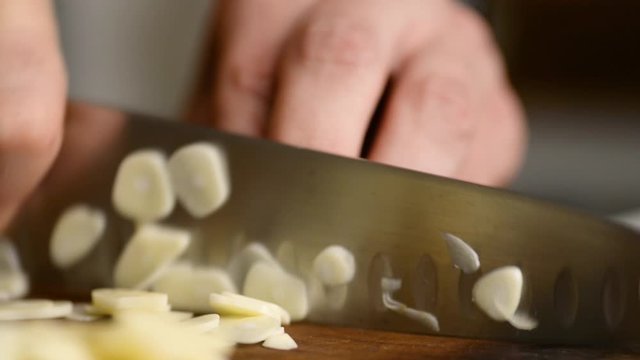 Extreme Close Up Of Chef Chopping And Slicing A Clove Of Garlic On A Wood Cutting Board